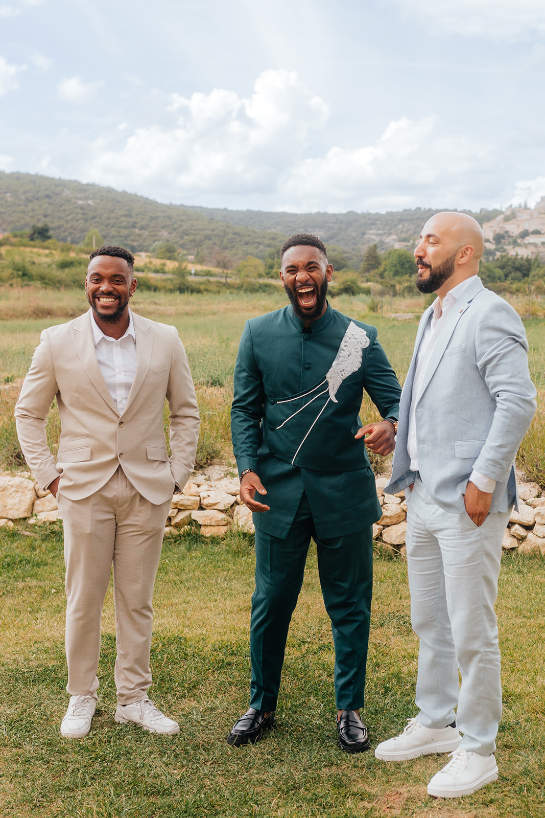 Trois hommes en costume posent joyeusement en extérieur, dans un cadre champêtre.