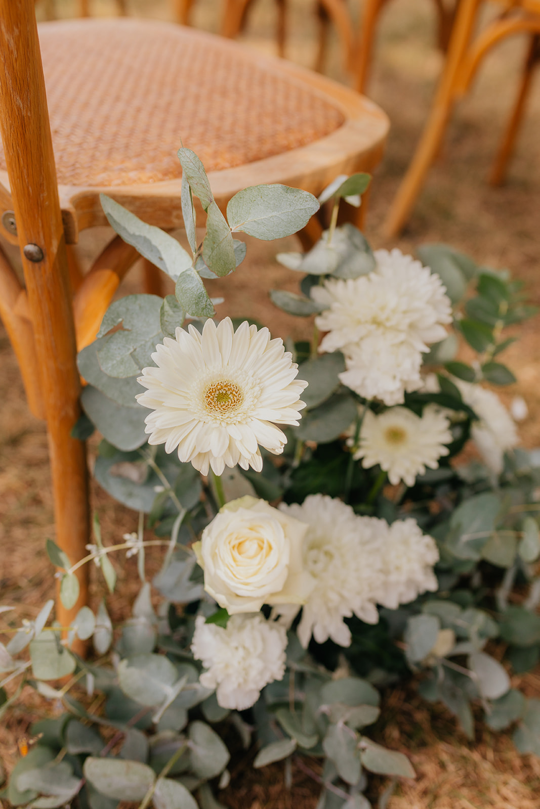 Bouquet de fleurs blanches posé sur une chaise en rotin dans un décor de mariage.