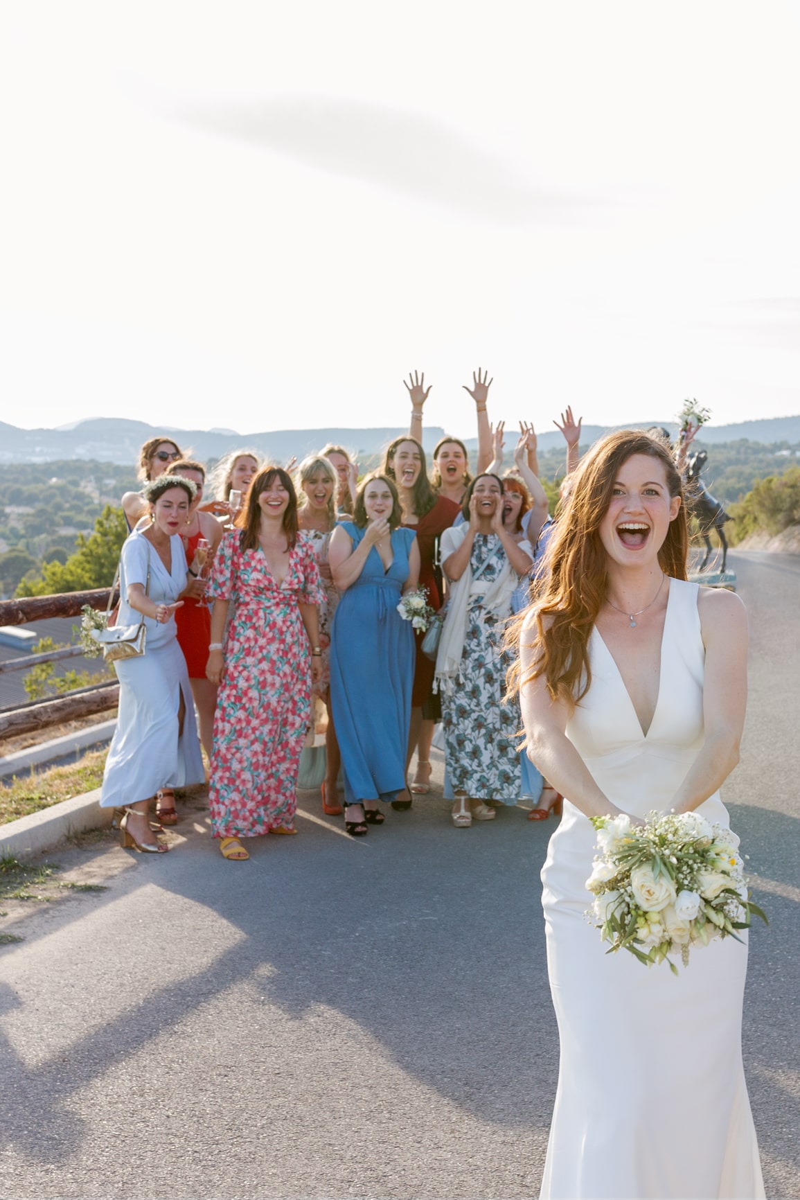 La mariée et ses demoiselles d’honneur s’amusent sur une route ensoleillée, dans une ambiance joyeuse.