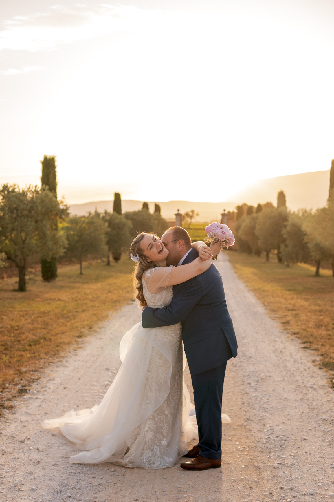 Les mariés s’enlacent sur un chemin en pleine nature, baignés par la lumière du soir.