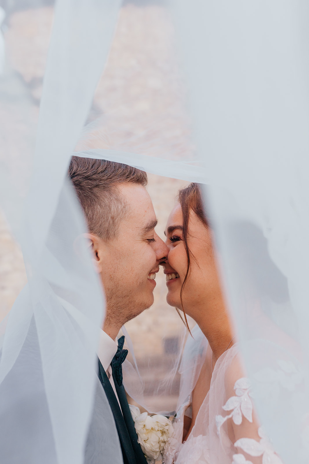 Les mariés échangent un moment complice sous le voile de la mariée, tendrement.