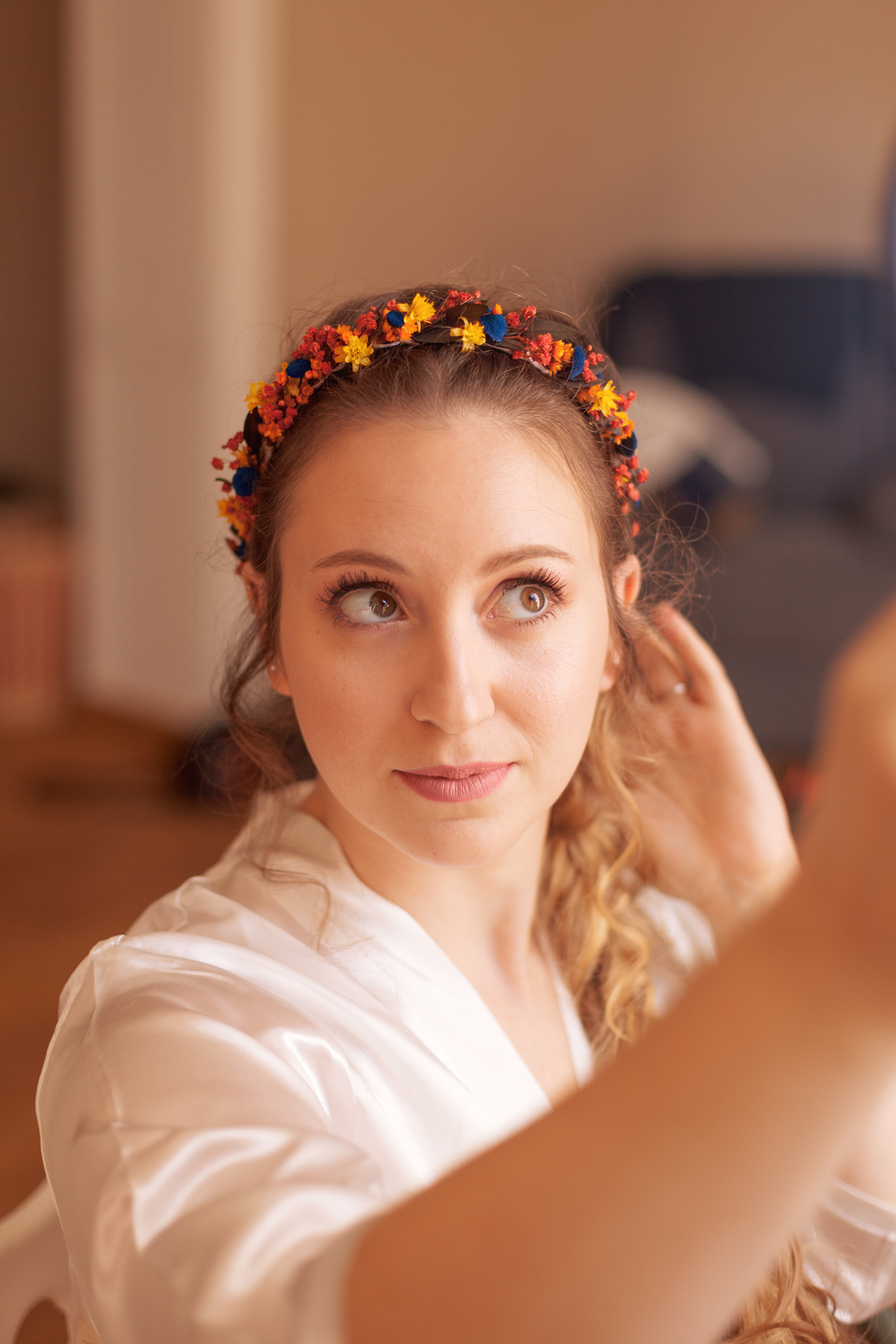 La mariée ajuste ses cheveux tout en portant une couronne de fleurs colorée.