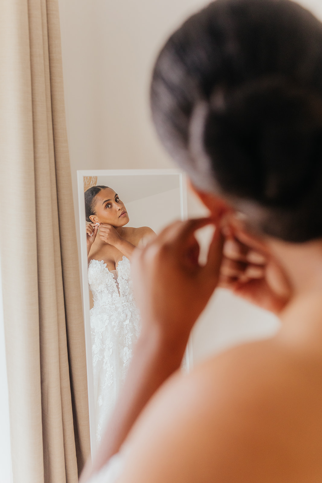 Vue de dos d’une mariée devant un miroir, en train de s’habiller.
