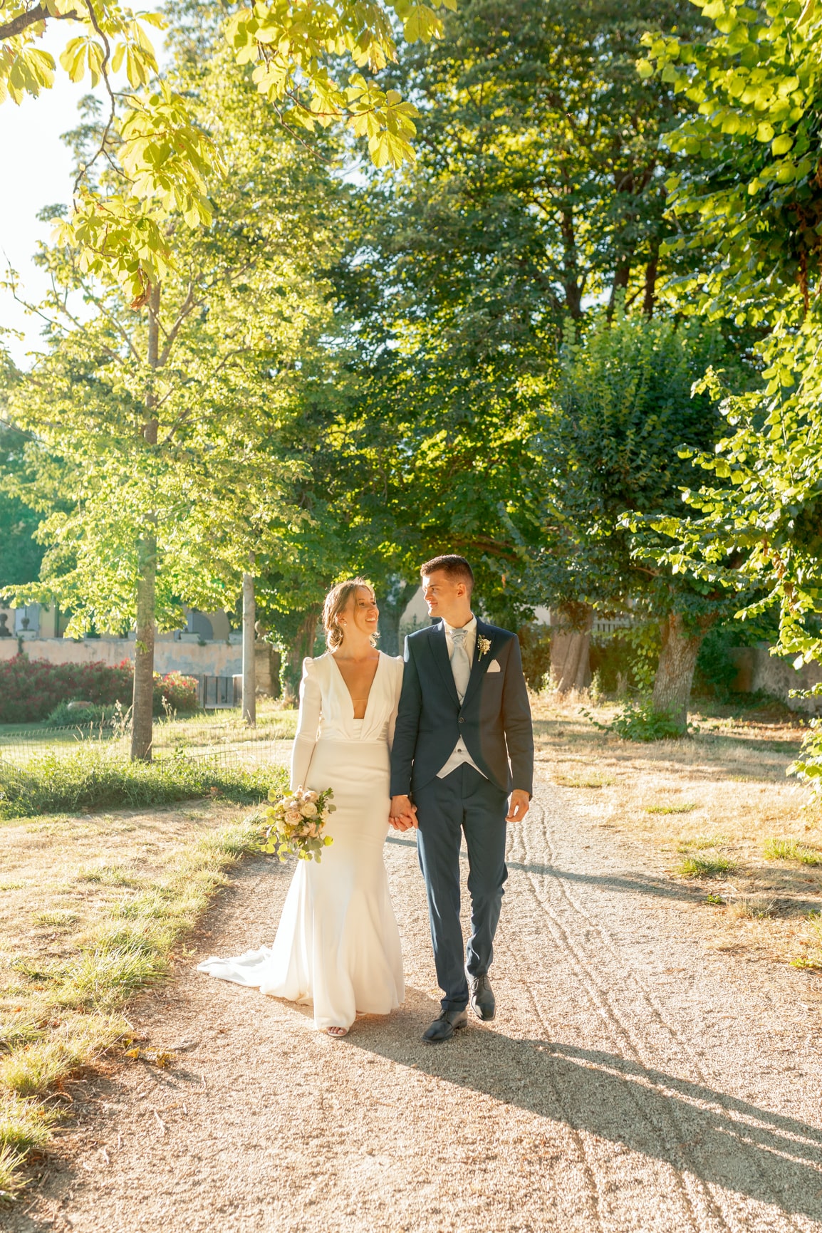 Les mariés marchent main dans la main dans une allée bordée d’arbres, après la cérémonie.